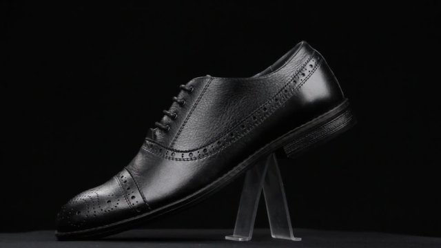 Rotation and approximation of black classic men's shoes on a black background. Copy space.