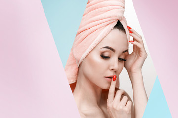 Portrait of young beautiful woman with healthy glow perfect smooth skin. Model with natural nude make up with pink towel on head look into the hole of pink, blue paper.