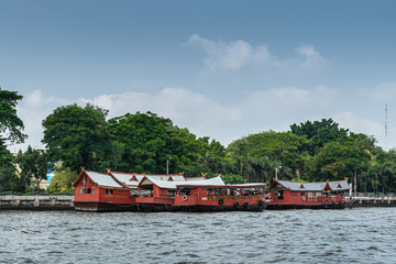 Bangkok city, Thailand - March 17, 2019: Chao Phraya River. Group of red barge boats on the water in front of park of Saifee Mosque under light blue sky.