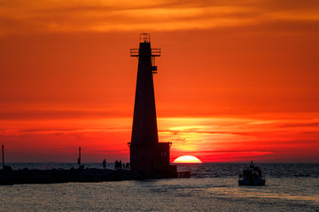 Fototapeta premium lighthouse at sunset with boat in channel