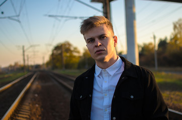 Fototapeta premium Businessman looking seriously at camera in sunset on the railroad outdoors