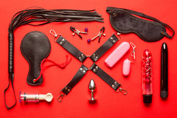 BDSM Kit from Sex shop. Leather whip, buttplug, vibrator, dildo, nipple clamps and other on red...