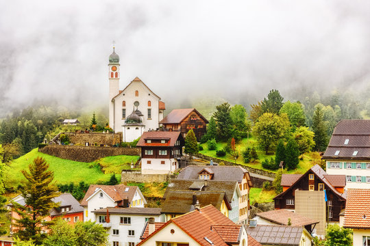 Wassen Alpine village in Switzerland. Beautiful autumn scenery of classical Swiss countryside with church and traditional houses among yellow-green foliage trees. Seasonal autumnal landscape with fog.