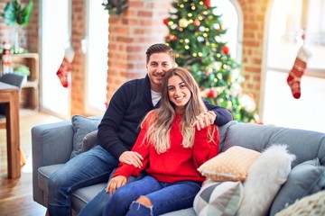 Obraz premium Young beautiful couple smiling happy and confident. Sitting on the sofa hugging around christmas tree at home
