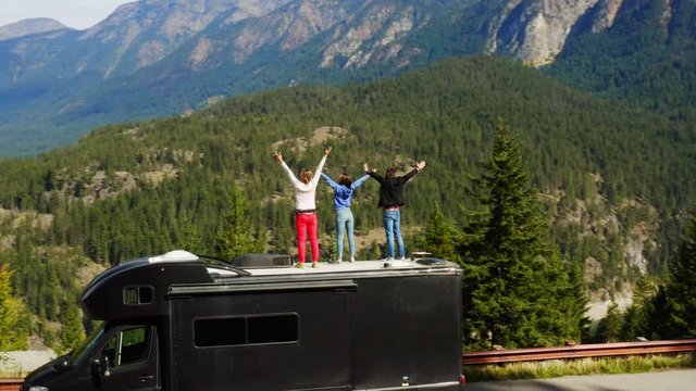Tourists standing on edge of cliff with breathtaking view, connection with nature, meditating at beautiful place, travel around USA on RV, aerial of endless forest and mountains