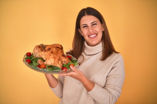 Young beautiful woman smiling proud holding thanksgiving turkey chicken on a tray over yellow background