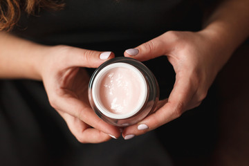 Beautiful woman hands with cream on dark background