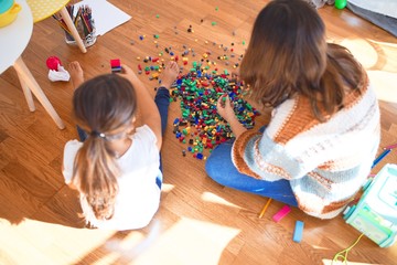 Beautiful teacher and toddler playing with building blocks toy around lots of toys at kindergarten