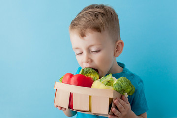 Boy holding basket with fresh vegetables on blue background. Vegan and healthy concept.