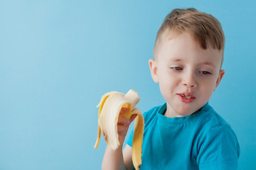 Little Boy Holding and eating an Banana on blue background, food, diet and healthy eating concept
