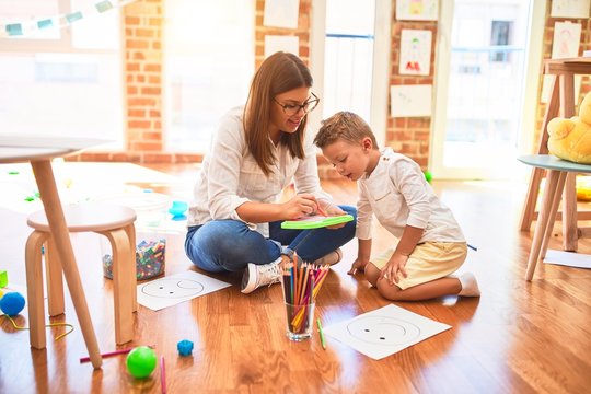 Beautiful teacher and toddler drawing using digital board around lots of toys at kindergarten