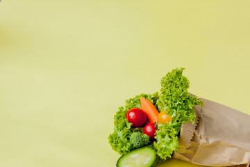Organic vegetables broccoli cucumbers bell peppers apples in brown paper Kraft grocery bag on yellow background. Healthy diet dietary fiber vegan plastic free concept. Poster banner