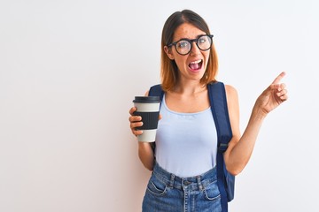 Beautiful redhead student woman wearing a backpack and drinking take away coffee very happy pointing with hand and finger to the side