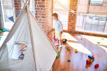 Beautiful blonde toddler holding tennis racket around lots of toys at kindergarten