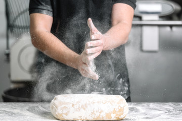 Baker claping hands with flour in restaurant kitchen .