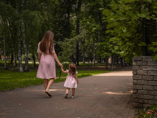 Mom and daughter walk and play in the park. Dressed in dresses. Sunny day, weekend in a city park.