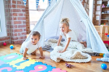 Beautiful toddlers playing inside tipi over blanket around lots of toys at kindergarten