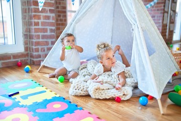 Beautiful toddlers playing inside tipi over blanket around lots of toys at kindergarten