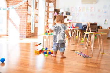 Adorable toddler playing with building blocks around lots of toys at kindergarten