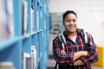 Fototapeta Waist up portrait of mixed-race college student wearing backpack and smiling at camera cheerfully while posing in library, copy space obraz
