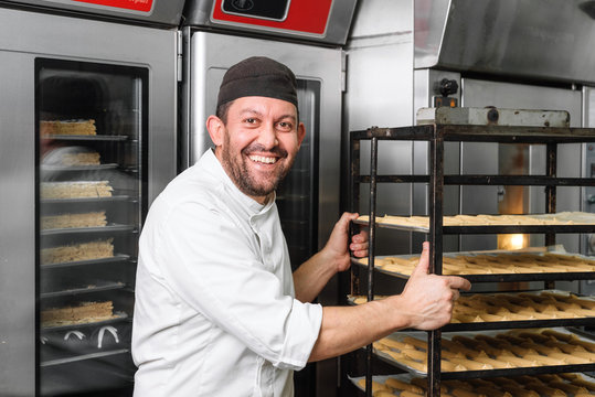 Baker Putting A Rack Of pastries Into Oven .