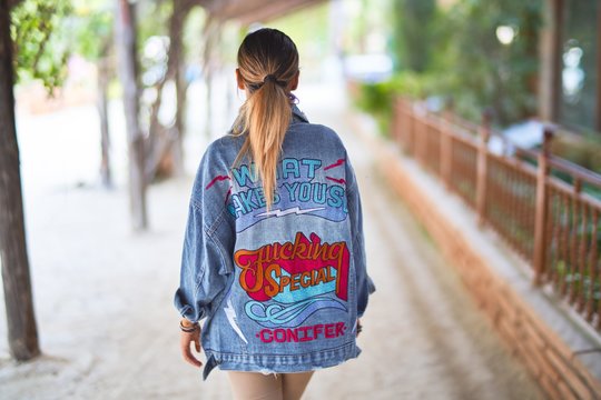 Young beautiful woman wearing denim jacket standing backwards at the town park
