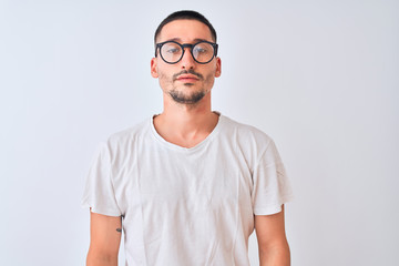 Young handsome man wearing glasses and standing over isolated background with serious expression on face. Simple and natural looking at the camera.