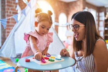 Young beautiful teacher and toddler learning maths playing with numbers puzzle at kindergarten