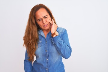 Middle age mature woman wearing denim jacket standing over white isolated background touching mouth with hand with painful expression because of toothache or dental illness on teeth. Dentist concept.