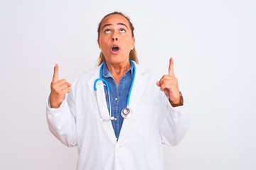 Middle age mature doctor woman wearing stethoscope over isolated background amazed and surprised looking up and pointing with fingers and raised arms.
