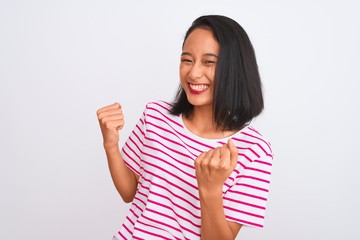 Young chinese woman wearing striped t-shirt standing over isolated white background very happy and excited doing winner gesture with arms raised, smiling and screaming for success
