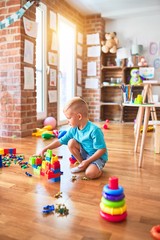 Fototapeta premium Young caucasian kid playing at kindergarten with toys. Preschooler boy happy at playroom.