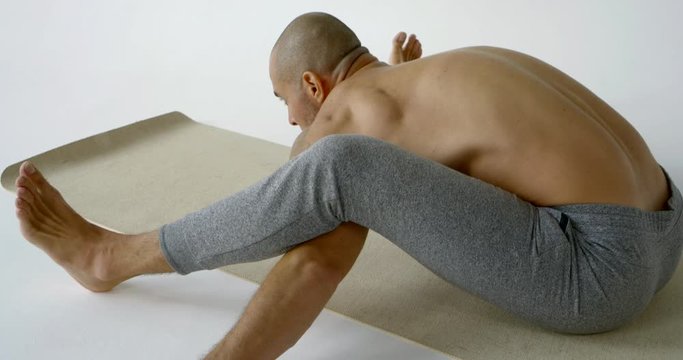 barefoot man in grey pants does kurmasana on mat slow motion