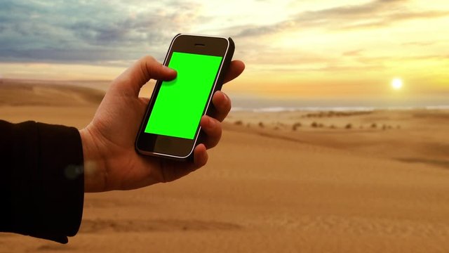 Male Hands Holding a Smart Phone Green Screen at the Beach with Sunset Sky. You can Replace Green Screen with the Footage or Picture you Want with “Keying” effect in AE (check out tutorials).