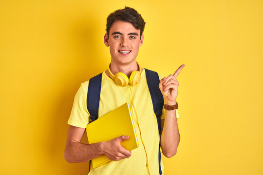 Teenager boy wearing headphones and backpack reading a book over isolated background very happy pointing with hand and finger to the side