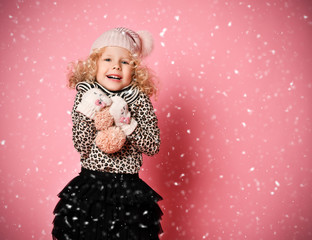 Christmas and New Year concept. Little baby girl in warm hat and gloves standing under snow with hands spread up 
