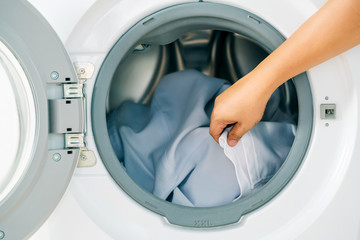 Close up man loading clothes into washing machine. Laundry concept.