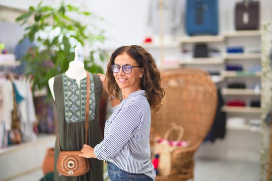 Middle age beautiful businesswoman smiling happy and confident preparing manikin at clothes shiop