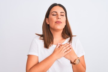 Naklejka premium Portrait of beautiful and young brunette woman standing over isolated white background smiling with hands on chest with closed eyes and grateful gesture on face. Health concept.