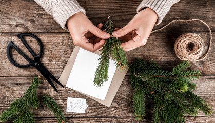 Woman hands decorates a Christmas card with fir branches on wooden background with scissors and...