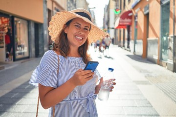 Young beautiful woman smiling happy walking on city streets on a sunny day of summer using smartphone