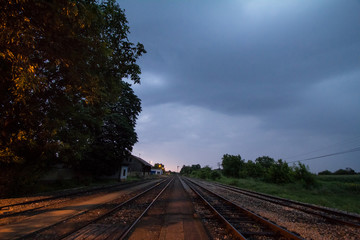 Fototapeta na wymiar Railway tracks, rails and platforms in a rural train station in Alibunar, Serbia, taken during sunset, after a cloudy and rainy storm with trees and a perspective