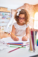 Beautiful toddler wearing glasses sitting drawing using paper and pencils at kindergarten
