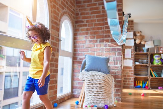 Beautiful toddler wearing glasses and unicorn diadem standing and smiling at kindergarten
