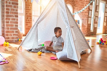 Beautiful african american toddler playing inside tipi smiling at kindergarten