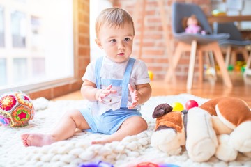 Beautiful toddler sitting on the blanket around lots of toys at kindergarten