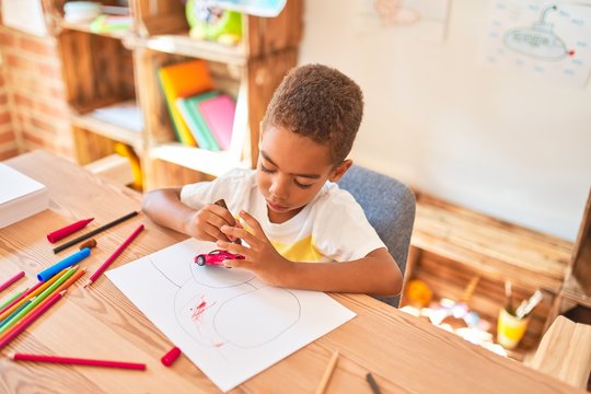 Beautiful african american toddler sitting painting car toy using marker pen on desk at kindergarten