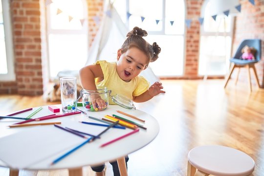 Beautiful toddler standing playing with chocolate colored balls on the table at kindergarten