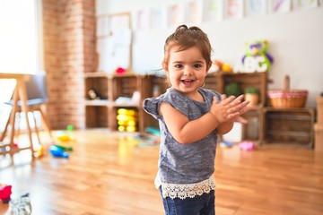 Beautiful toddler standing on the floor applauding and smiling at kindergarten - obrazy, fototapety, plakaty