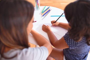 Beautiful teacher and toddler girl drawing draw using colored pencils at kindergarten